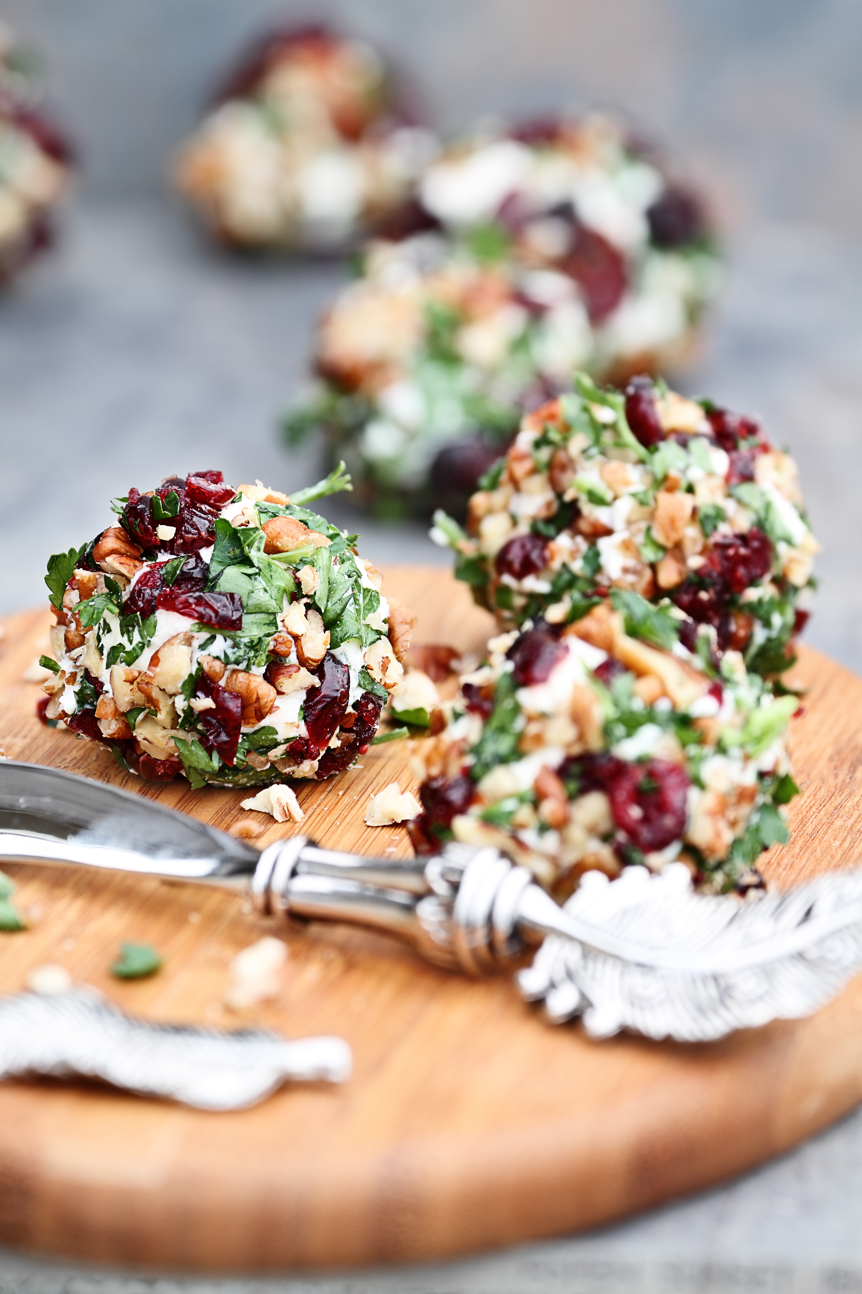 Cranberry nut cheeseball made with cream cheese, goat or feta cheese, parsley, cranberries and chopped pecans over a rustic background. Extreme shallow depth of field with selective focus on center cutting board.